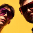 24.Avēnija - Music Duo: Two men, Ernests Vīgners and Kārlis Grīnbergs, standing with sunglasses against a vibrant yellow background, both looking straight to the camera.